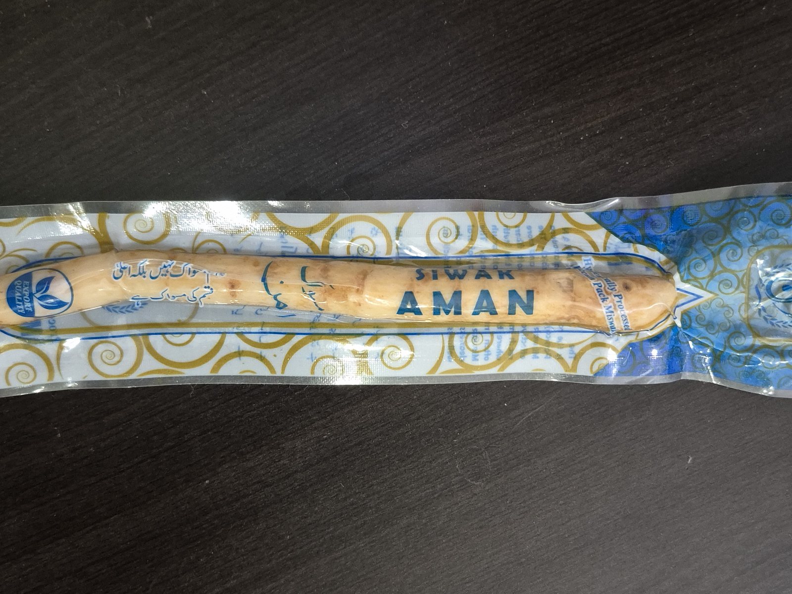 A miswak stick in its sealed vacuum pack, lying on a wooden table