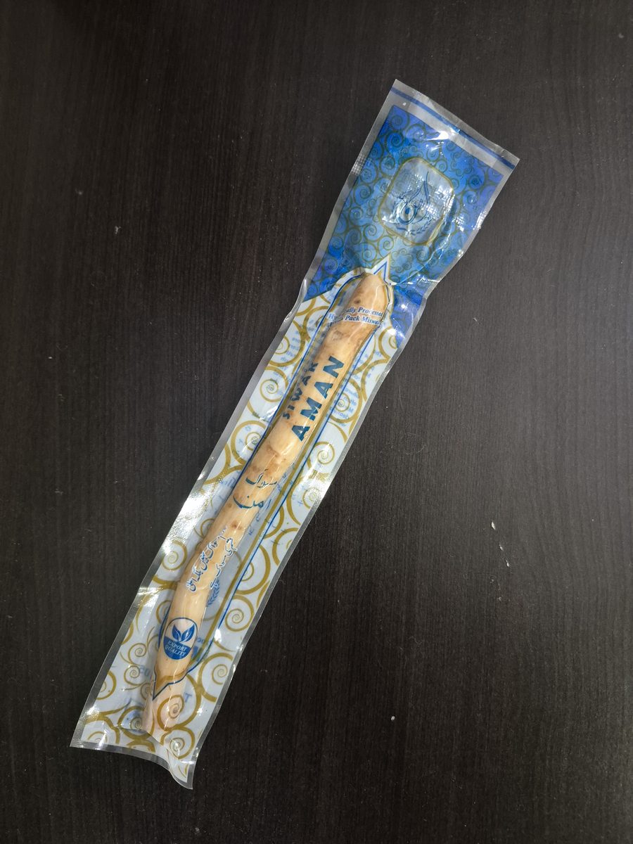 One miswak stick sealed in its clear vacuum pack, on a dark wood table